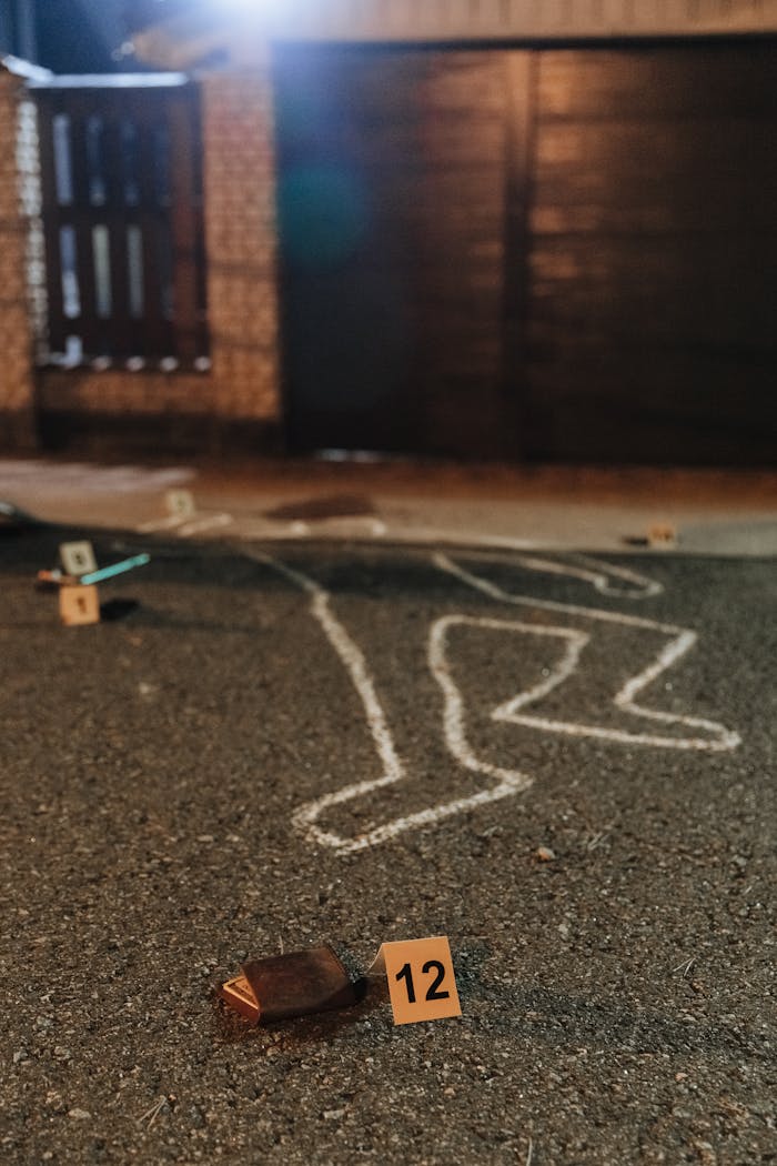 Chalk outline and evidence markers at a crime scene outdoors at night.